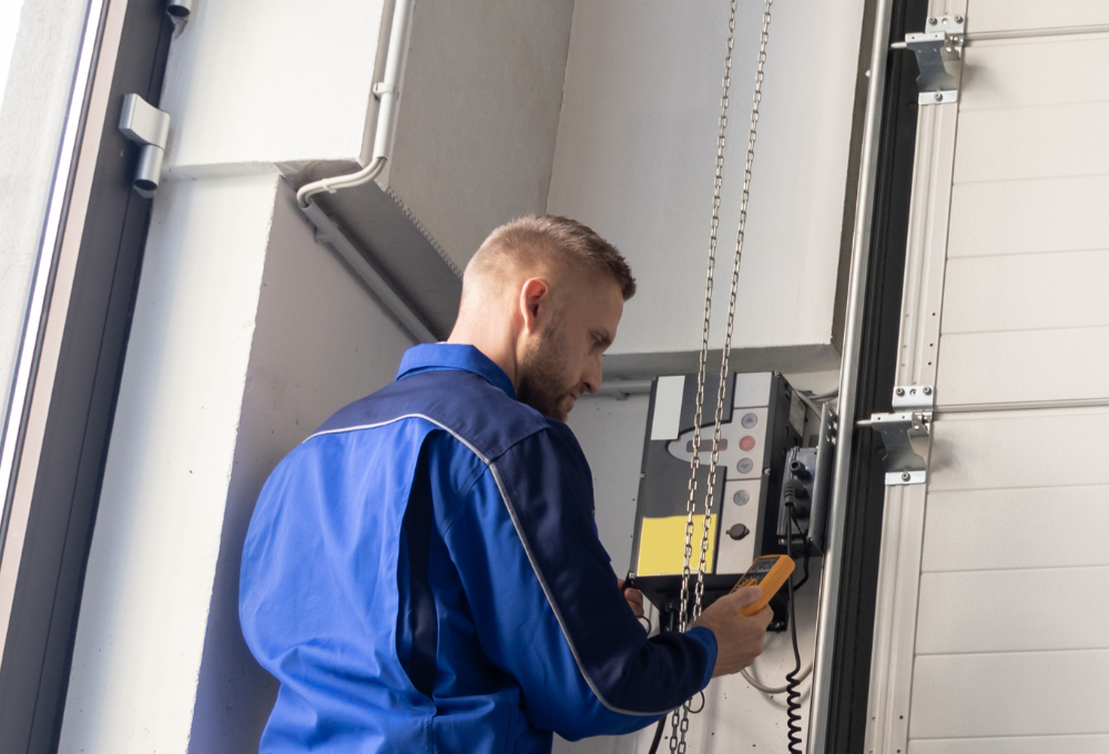 A man in a blue work uniform operates a control panel mounted on an industrial door mechanism.